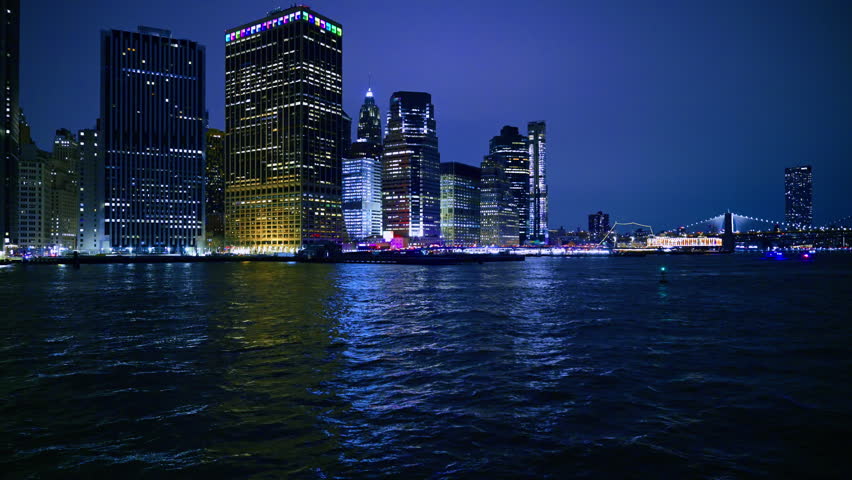 New York financial district skyline and Brooklyn Bridge at night. View of Lower Manhattan skyscrapers and illuminated suspension bridge over the East River.