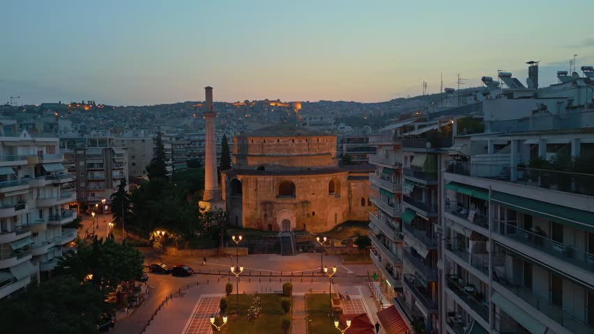 Aerial drone flight towards the illuminated historic Rotunda monument in Thessaloniki, Greece, during twilight.
