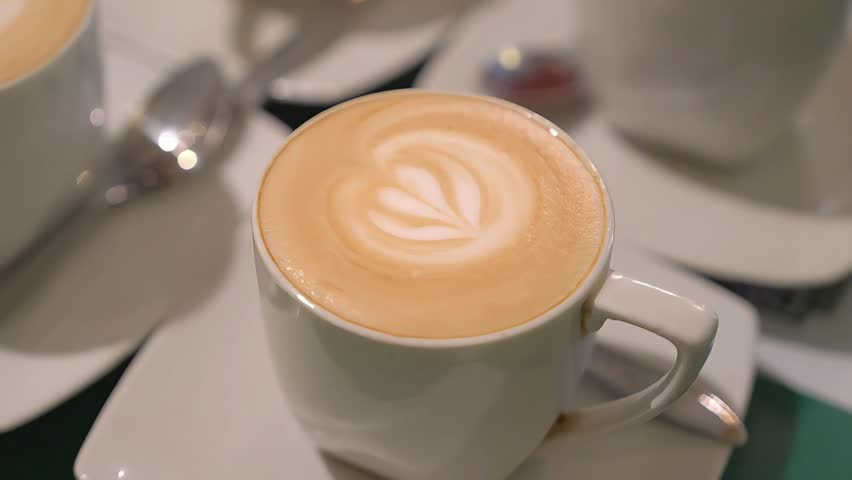 Hot cappuccino with latte art in a white cup, close-up cafe coffee drink with creamy foam and warm bokeh background