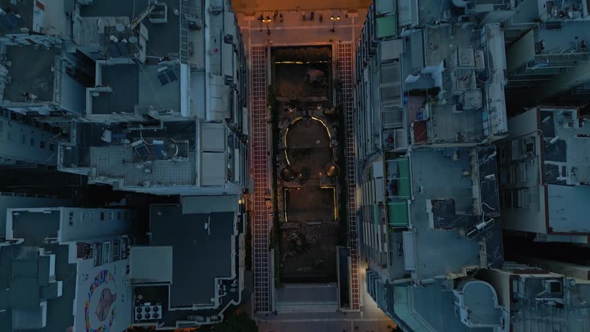 Aerial top-down view over Navarino Square ruins, tilting up to reveal the illuminated historic Rotunda monument in Thessaloniki, Greece at night.