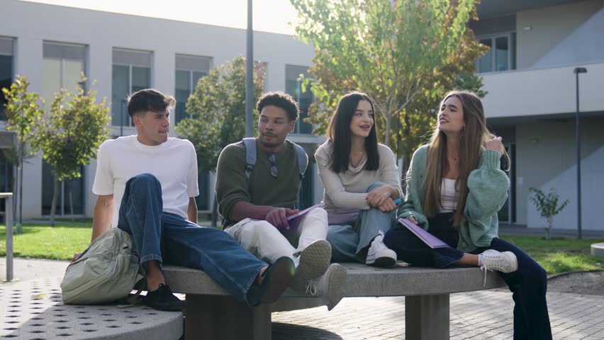 Four multicultural friends sitting together on a bench at the university campus. Young male and female students talking and relaxing outdoors