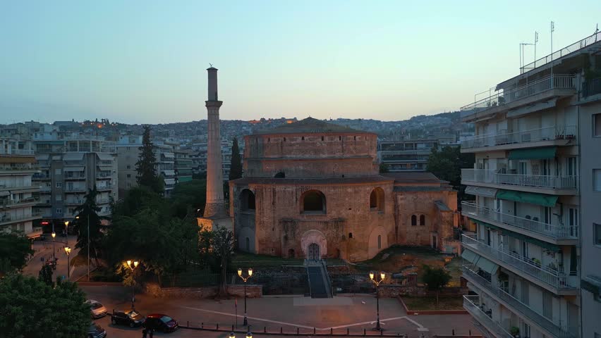 Aerial evening view of the illuminated historic Rotunda monument and its minaret in Thessaloniki, Greece, during twilight.