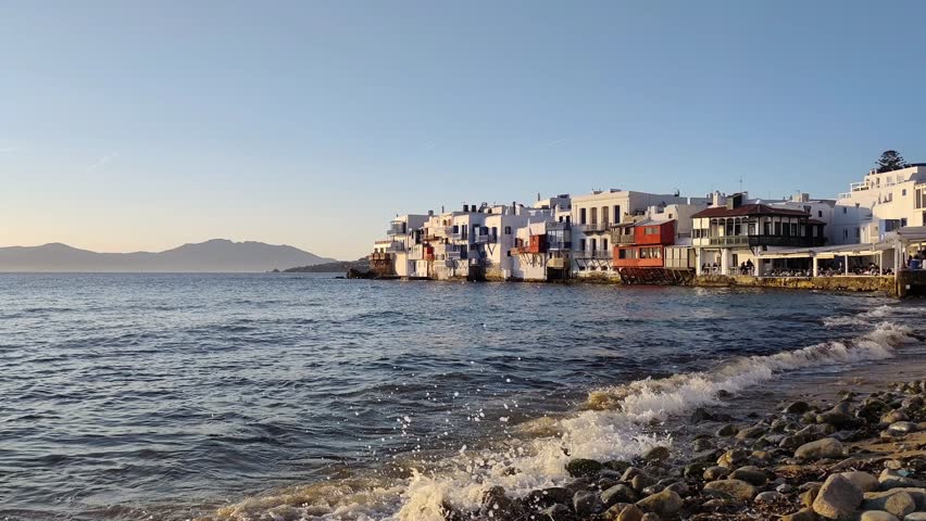 MYKONOS, GREECE - MAY 6TH 2026: Breathtaking dusk view of Little Venice—locally known as Alefkandra—one of the most romantic and spirited corners of the Cyclades. Nestled on the western edge of Mykonos Town, this dreamlike neighborhood is famous for its 18th-century homes perched right at the water’s edge, their vibrant wooden balconies suspended like works of art over the crashing waves of the Aegean.