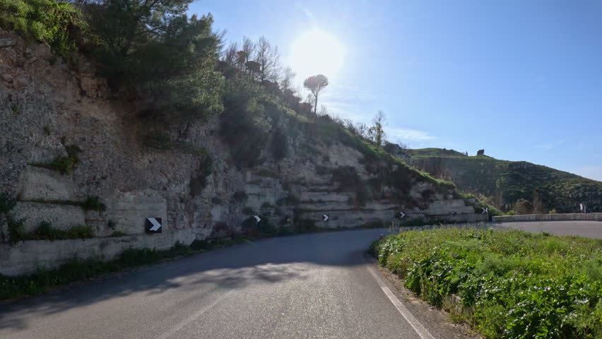 LENS FLARE: Panoramic drive down a winding road above Mediterranean Sea with scenic view of mountains, bay and coastal towns on sunny day. Picturesque landscape while traveling in western Sicily.