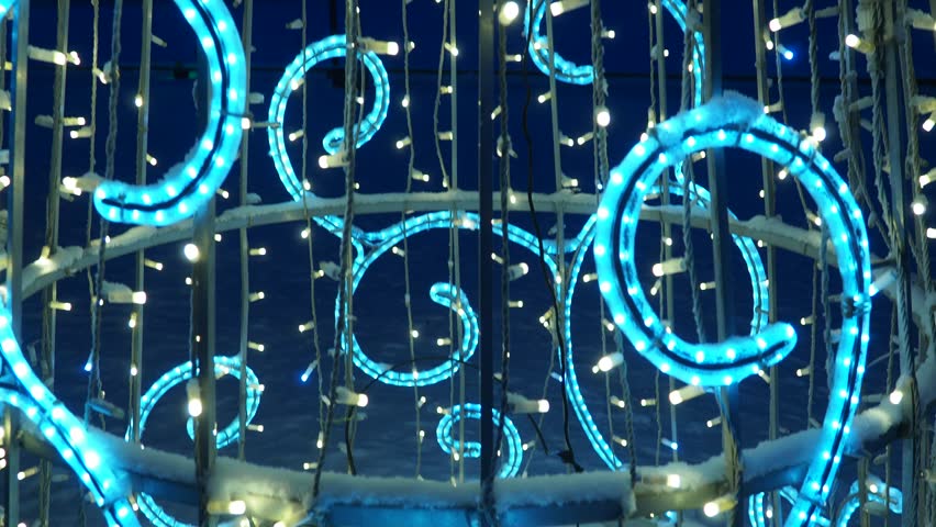 Colorful garland lights are wrapped around a Christmas tree. The lights glow brightly in the night sky. The tree stands tall, adding joy to the festive season.