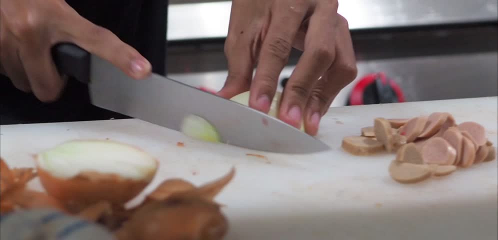 Close-up of hands skillfully slicing onions on a kitchen cutting board.