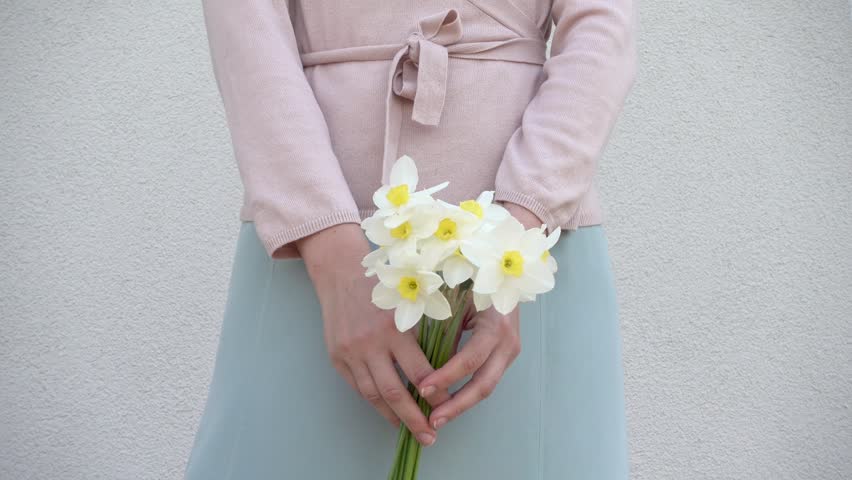 Cute woman holds a vibrant bouquet of yellow daffodils, symbolizing spring renewal. Soft pastel dress and minimalist background enhance the fresh, joyful atmosphere. Ideal for seasonal campaigns
