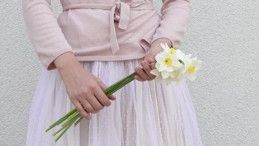 Cute woman holds a vibrant bouquet of yellow daffodils, symbolizing spring renewal. Soft pastel dress and minimalist background enhance the fresh, joyful atmosphere. Ideal for seasonal campaigns