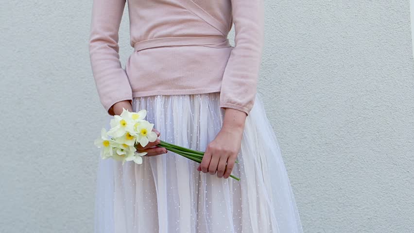 Cute woman holds a vibrant bouquet of yellow daffodils, symbolizing spring renewal. Soft pastel dress and minimalist background enhance the fresh, joyful atmosphere. Ideal for seasonal campaigns