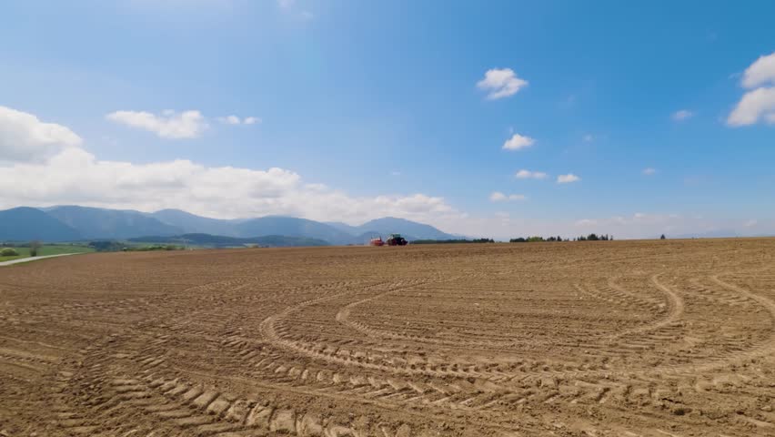 Agricultural landscape with a freshly plowed field, tire marks, and mountains in the background