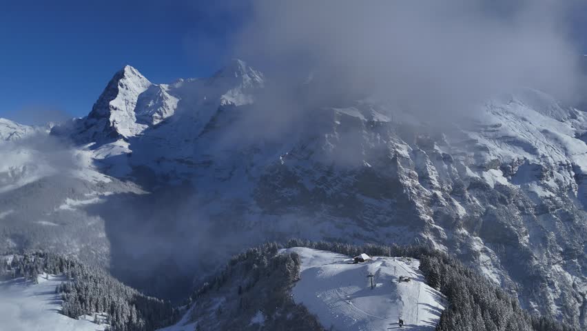 Drone perspective over snow-covered alpine ridges and forests under winter clouds in the Bernese Oberland, Switzerland.