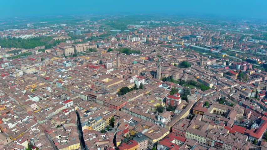 4K aerial view of Parma historic centre with Romanesque cathedral, octagonal baptistery, Palazzo della Pilotta and dense terracotta rooftops stretching across the Po Valley in Italy.