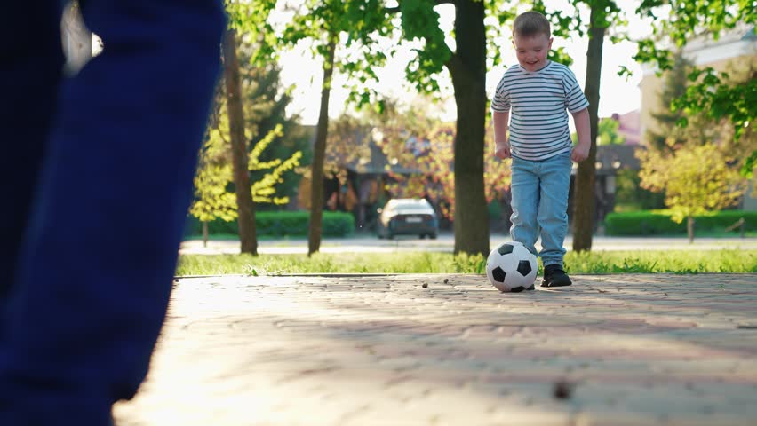 Child kicks football, dad son plays soccer. Dad kid boy play soccer together park summer. Happy family plays soccer weekend. Family fun kicking football park. Family sports soccer team plays outdoors
