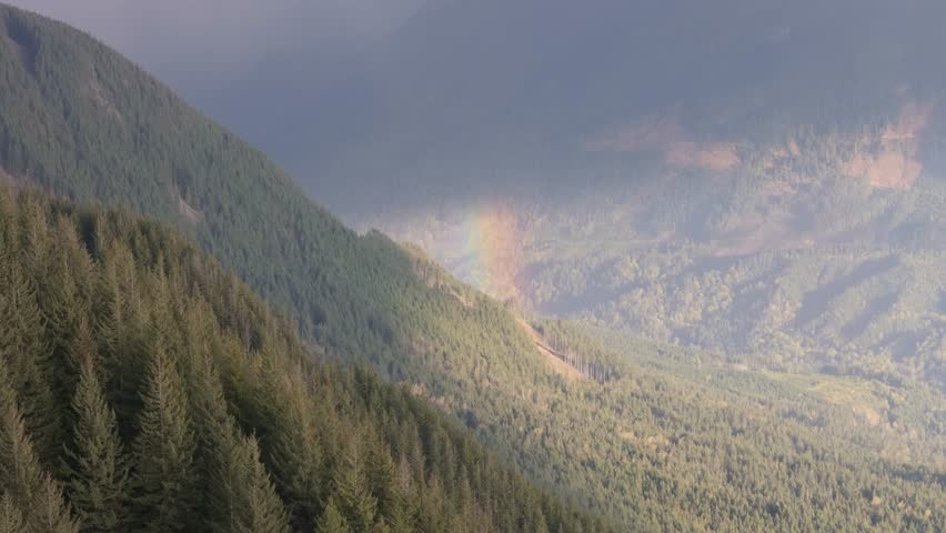 Vibrant Rainbow Arches Over Lush Forested Mountains In British Columbia, Canada