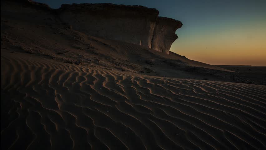 Traveling shot across textured sand dunes and limestone rock formations in Zekreet, Qatar, with changing sunlight in arid desert landscape