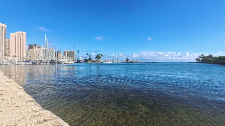 Honolulu, USA - Overview of the Ala Wai Boat Harbor showing clear water and docked boats under a blue sky near Waikiki.