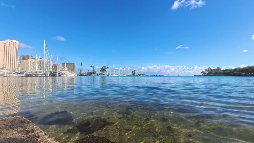 Honolulu, USA - View of the Ala Wai Boat Harbor with calm waters and several boats docked at the marina in Honolulu, Hawaii. Tall buildings are visible in the background.