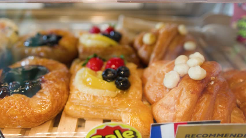 Slow camera pan across a glass display case filled with fresh fruit danishes and buns