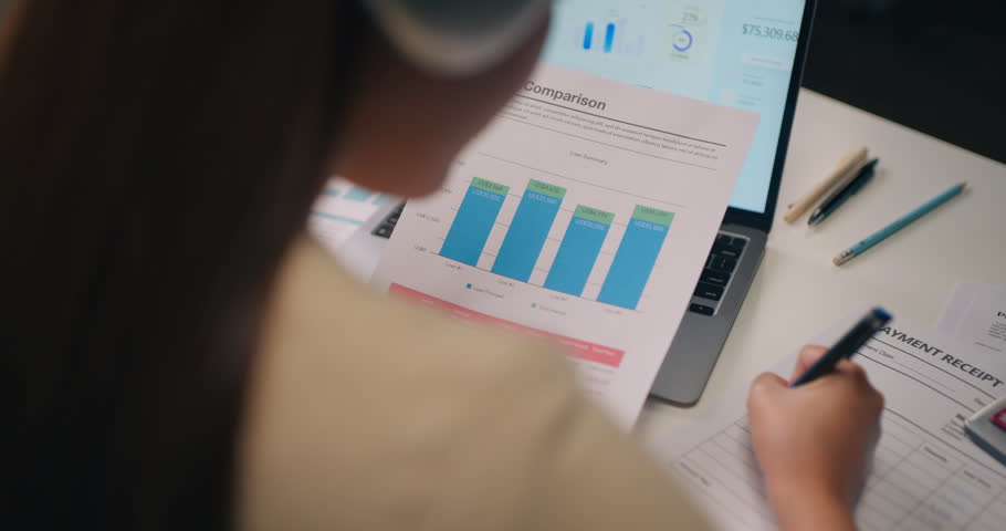 Close-up of female holding loan comparison paper with bar graph and calculator on desk. Mortgage planning, debt analysis, and financial investment research.