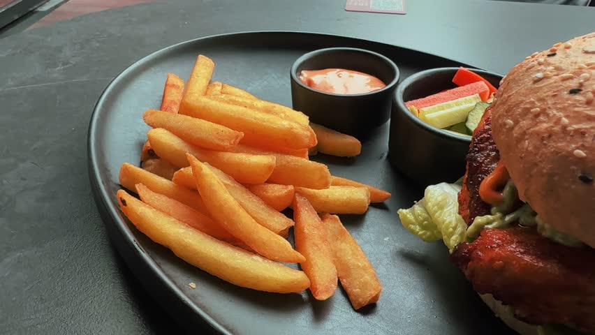 Burger with French Fries and Dipping Sauce on Dark Plate in Restaurant