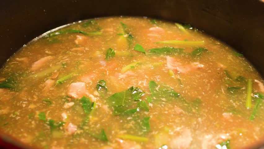 Steam rises from a bubbling seafood soup with green herbs inside a dark iron pot