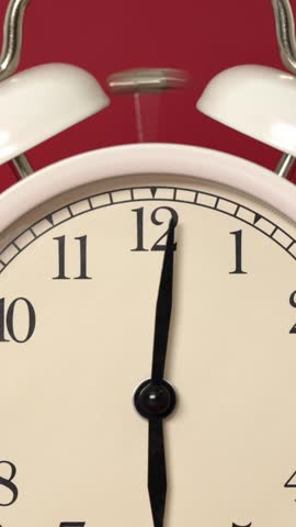 Close-up of a classic white alarm clock with a retro dial ringing loudly against a red background, with the hammer shaking between the two bells and the hands pointing to six o
