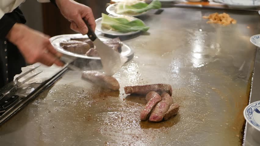POV to kobe sirloin wagyu steak while cooking on teppan yaki flat pan in japanese style restaurant for lunch time. Chef cooking wagyu kobe beef sirloin steak on teppanyaki flat pan