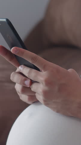 Vertical Screen : Young Asian Pregnant woman use mobile phone search pregnancy information. Mom feel happy smile positive peaceful while take care child lying on sofa in living room at home concept.