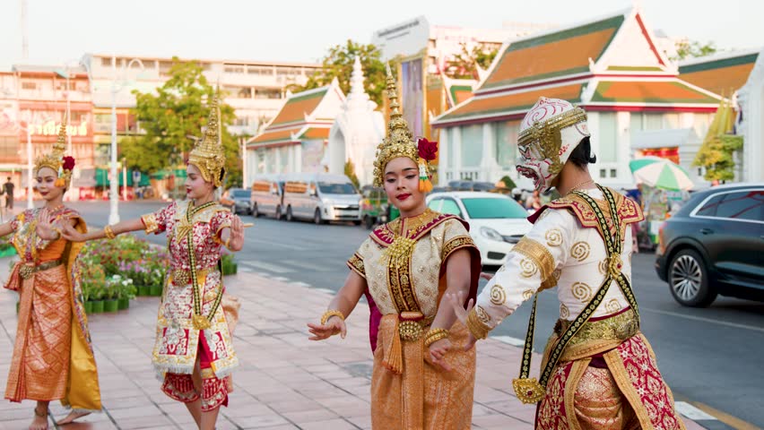 Performers in ornate golden costumes dance outdoors near a historic temple in Bangkok, Thailand