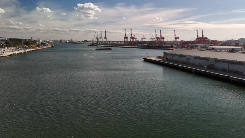 Melbourne Docklands and the Yarra River as barges and boats cruise the river and cranes busy themselves in the background with the city and the Bolte Bridge close by. 