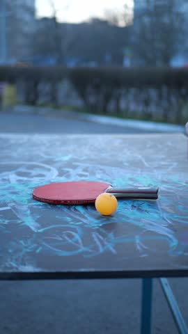 Hands playing table tennis with red paddle and orange ball on graffiti street table