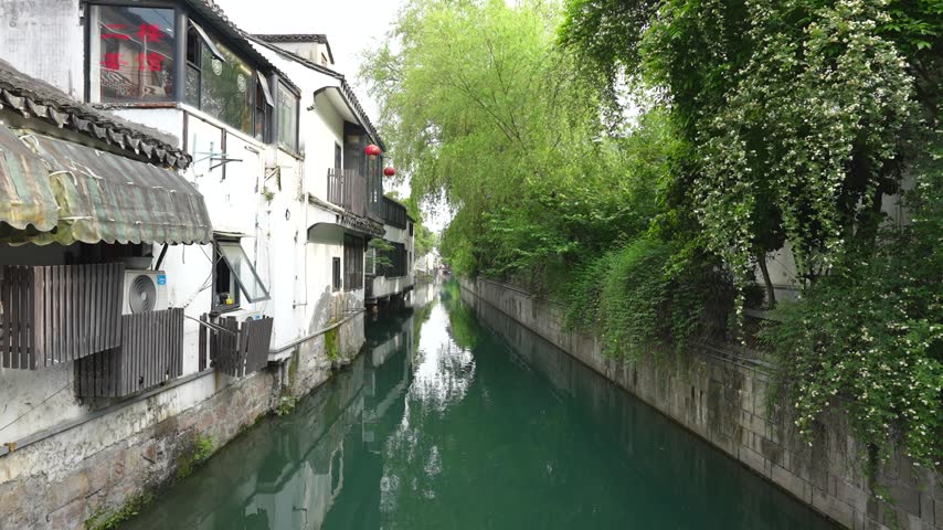 Calm waters of a canal reflecting traditional houses and lush greenery in Suzhou, the Venice of China