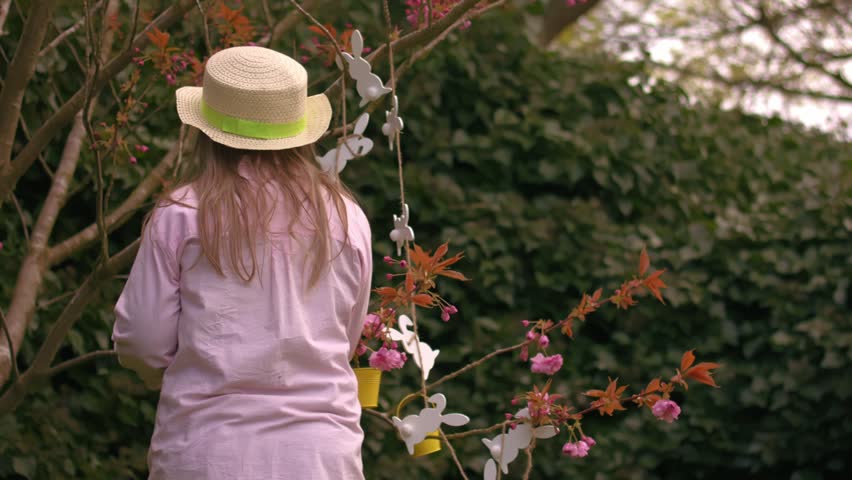 Woman wearing Easter bonnet and sits by easter decorations on blossom tree medium zoom slow motion shot selective focus