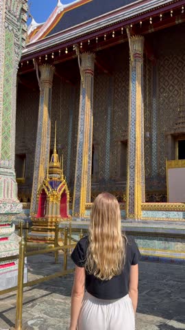 Woman walking inside Grand Palace complex near Wat Phra Kaew in Bangkok, Thailand. Traditional Thai temple architecture and cultural travel experience in Southeast Asia.