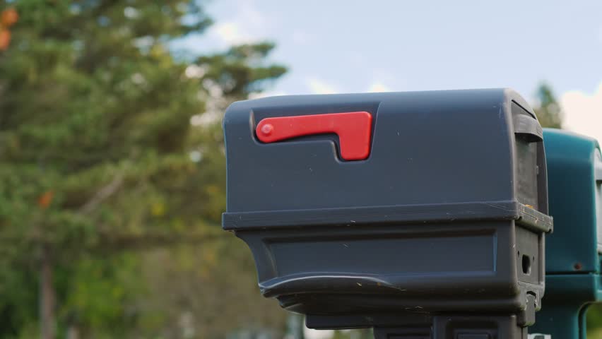Woman puts paper mail in a mailbox on a sunny day. Person sending a letter into a mailbox. Female hand putting a message into a modern mailbox. Cinematic slow-motion footage of mail delivery.