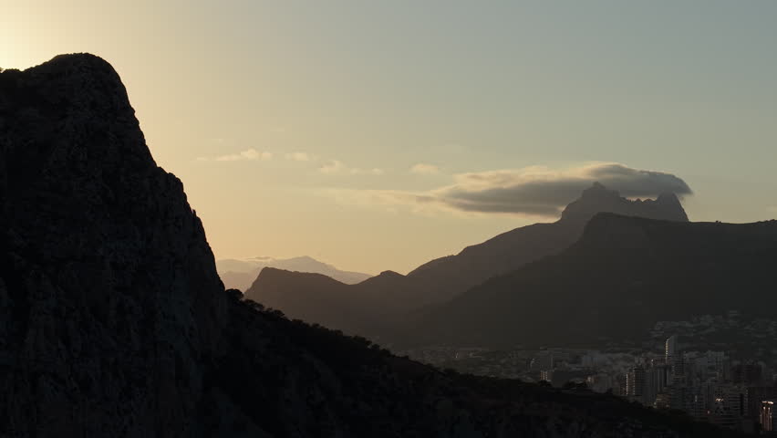Sunrise behind Penon de Ifach with mountain silhouettes and Calpe skyline aerial landscape Spain.