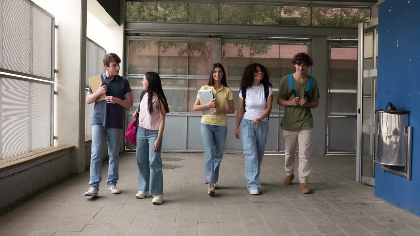 Group of multi-ethnic high school students walking together in a school hallway with books and laptops