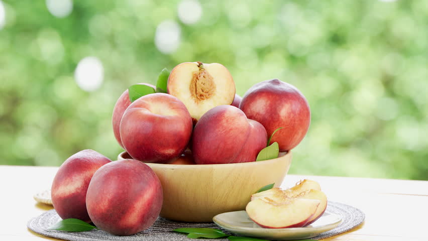 Red peach in wooden bowl on blurred greenery background, Peach fruit in wooden bowl on wooden table in garden.