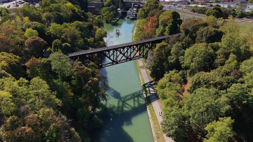 Aerial view of historic railway bridge over Erie Canal in Lockport, New York, USA with boat approaching locks and autumn forest.