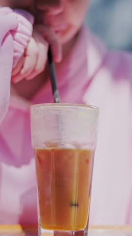 Iced espresso orange juice drink in glass with straw on table. Woman sitting in cafe drinking coffee cocktail. Refreshing summer beverage, break time and lifestyle activity.