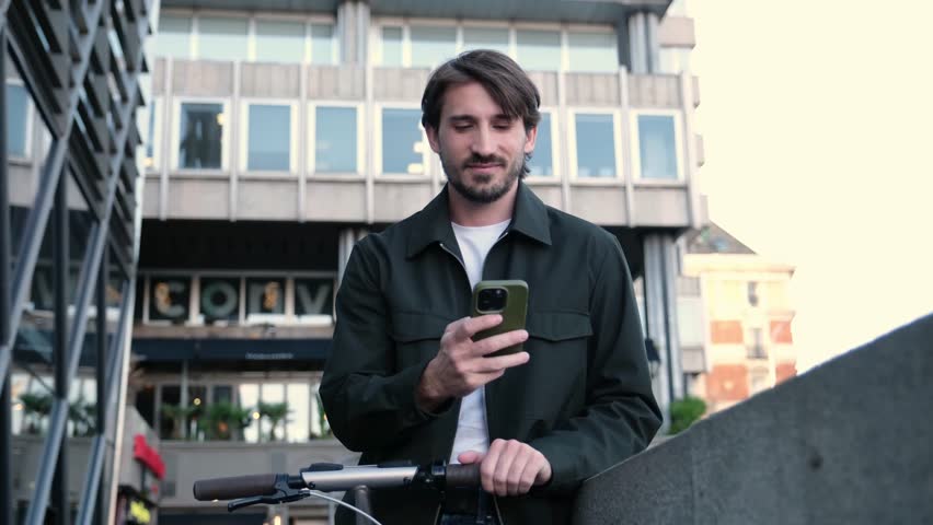 Modern man with an electric scooter checks his mobile phone while standing in an urban environment