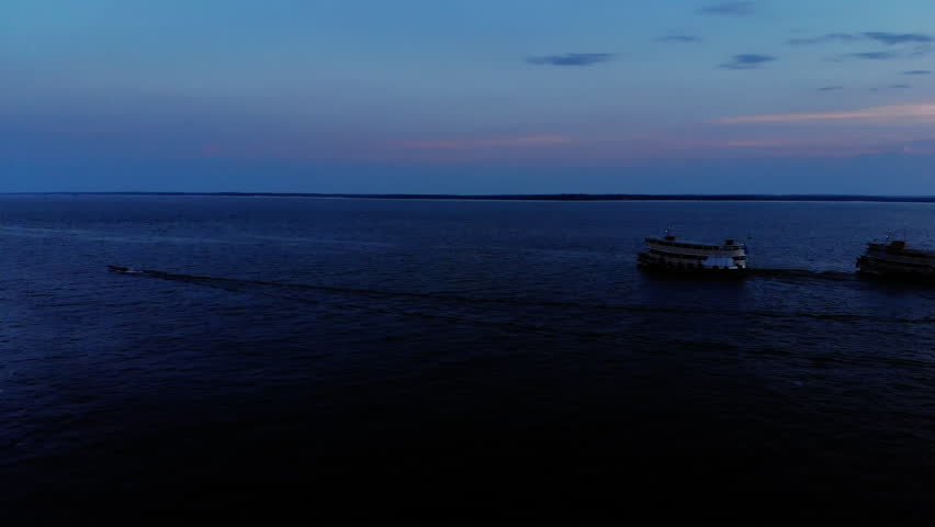 Calm river landscape at dusk with distant boats and deep blue water, showing peaceful atmosphere, navigation activity and natural evening scenery