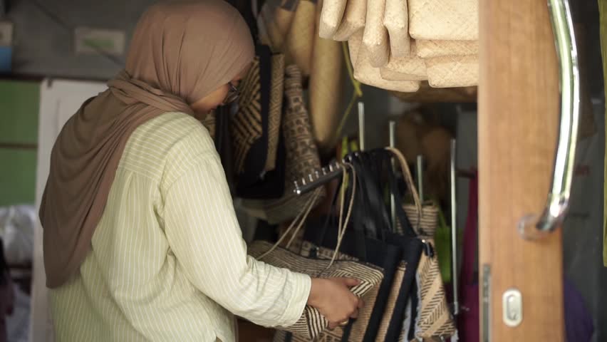 Female customer examining handmade rattan bag in artisan shop, concept of small business, local craftsmanship and sustainable consumer choice