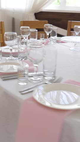Beautifully decorated round banquet table featuring white tablecloth pink textile napkins porcelain plates crystal wine glasses and polished silverware arranged for formal wedding reception celebration.