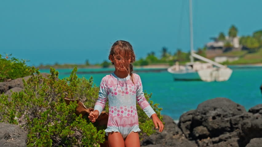 A cute little girl is happily walking along the ocean shore with beautiful turquoise water. Happy, active, childhood