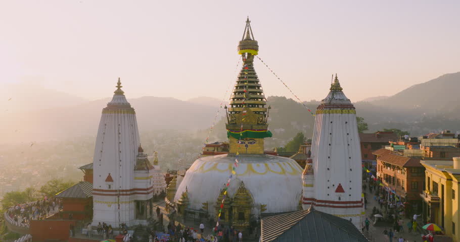 An aerial pull-out view revealing Swayambhunath Monkey Temple and Kathmandu Valley, Nepal, during golden sunset light with a golden sky and urban city.