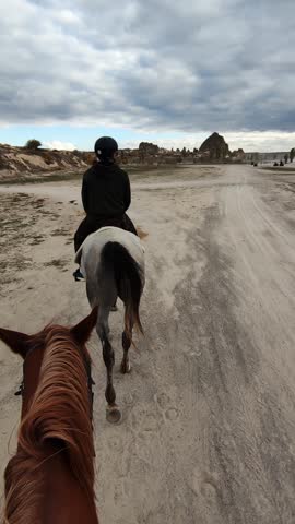 Personal perspective of a man riding a horse in meadow with hills and mountains on background. vertical shot of group of tourists on equestrian walk at cloudy spring day. active leisure time in