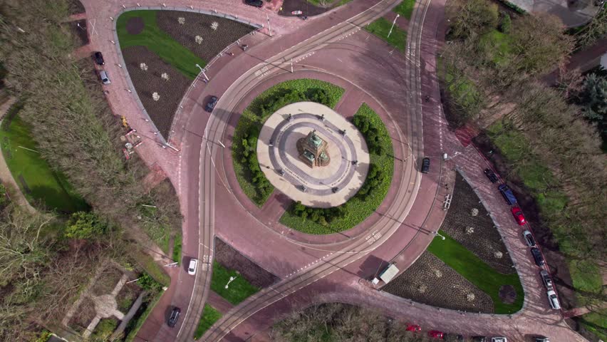 Top down aerial in Dutch capital The Hague, The Netherlands with lush greenery park around historic monument forming the center of an intersection crossroad