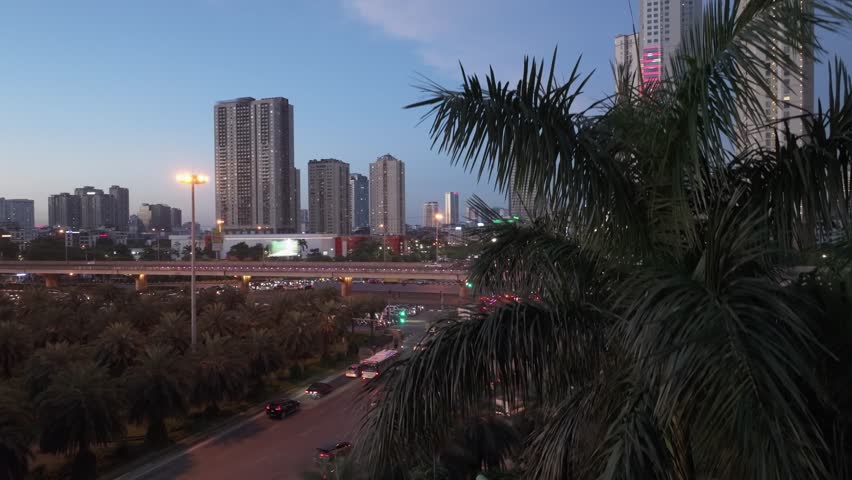 Blue hour drone view of Hanoi intersection with illuminated traffic, elevated highway, and dense residential skyline at dusk.
