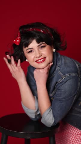 A girl in a beautiful pin-up style dress in a denim jacket with an incredible smile blown by the wind on a dark red background